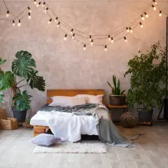 Przytulna sypialnia boho loft z łóżkiem, roślinami i girlandą świetlną.