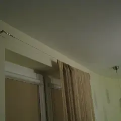 Elegancka zasłona w beżowym kolorze wisi na cienkiej lince zamiast karnisza, tworząc minimalistyczny wygląd.